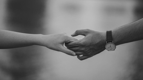Black and white photo of two people reaching out and clasping hands, symbolizing a couple supporting each other through addiction recovery.
