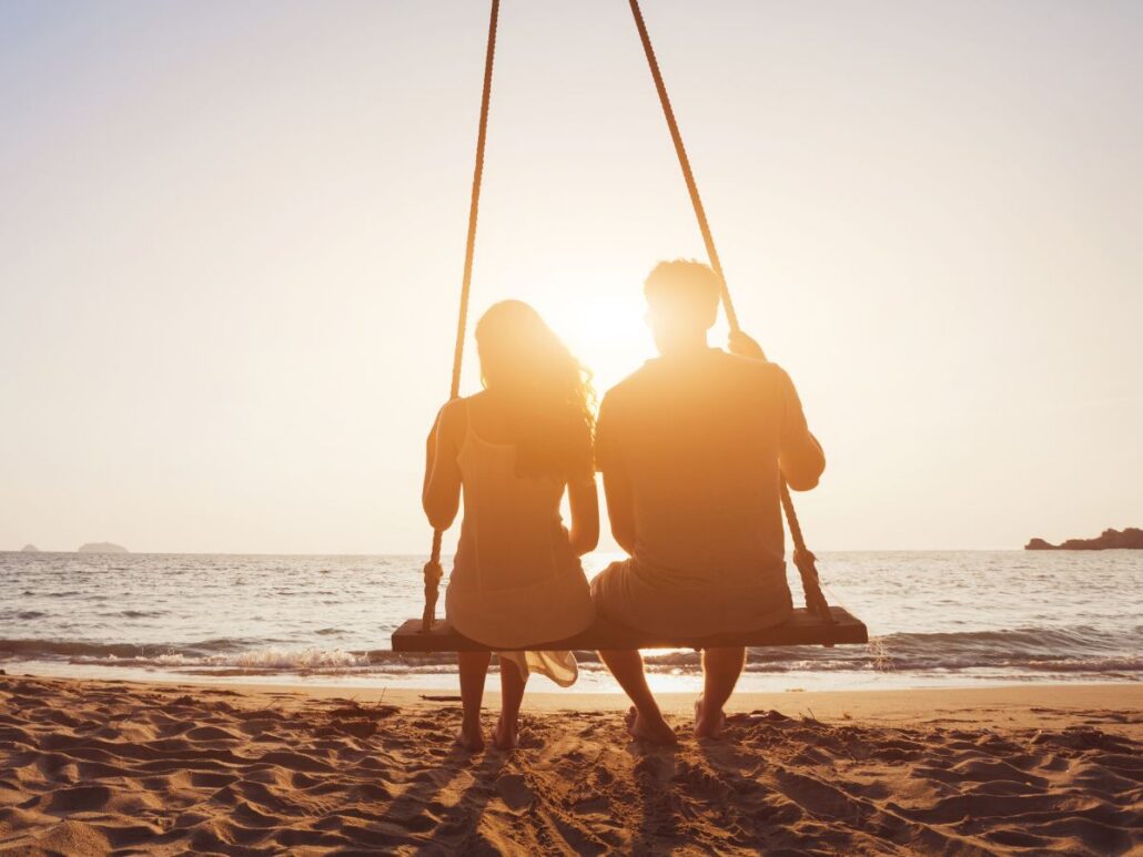 A couple sitting together on a Long Island shoreline at sunrise, reflecting calmly as they consider treatment and recovery options